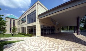 施設の建物外観。2階建ての明るい色合いの建物で、ポーチと広い駐車スペースが見える。